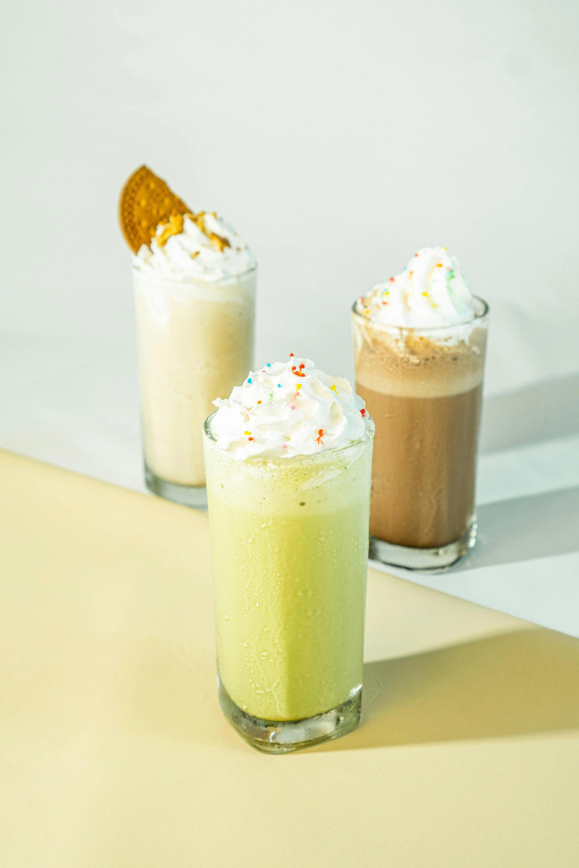 Matcha Frappe im Glas mit Sahne und Streuseln, im Hintergrund andere Frappe Getränke