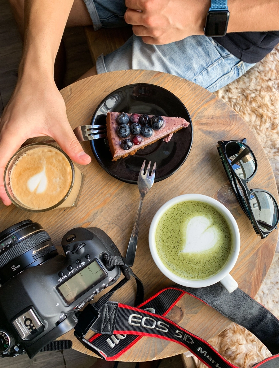 Cafétisch mit Matchatasse, Kuchen, Cappuccino und einer Kamera im Sommer
