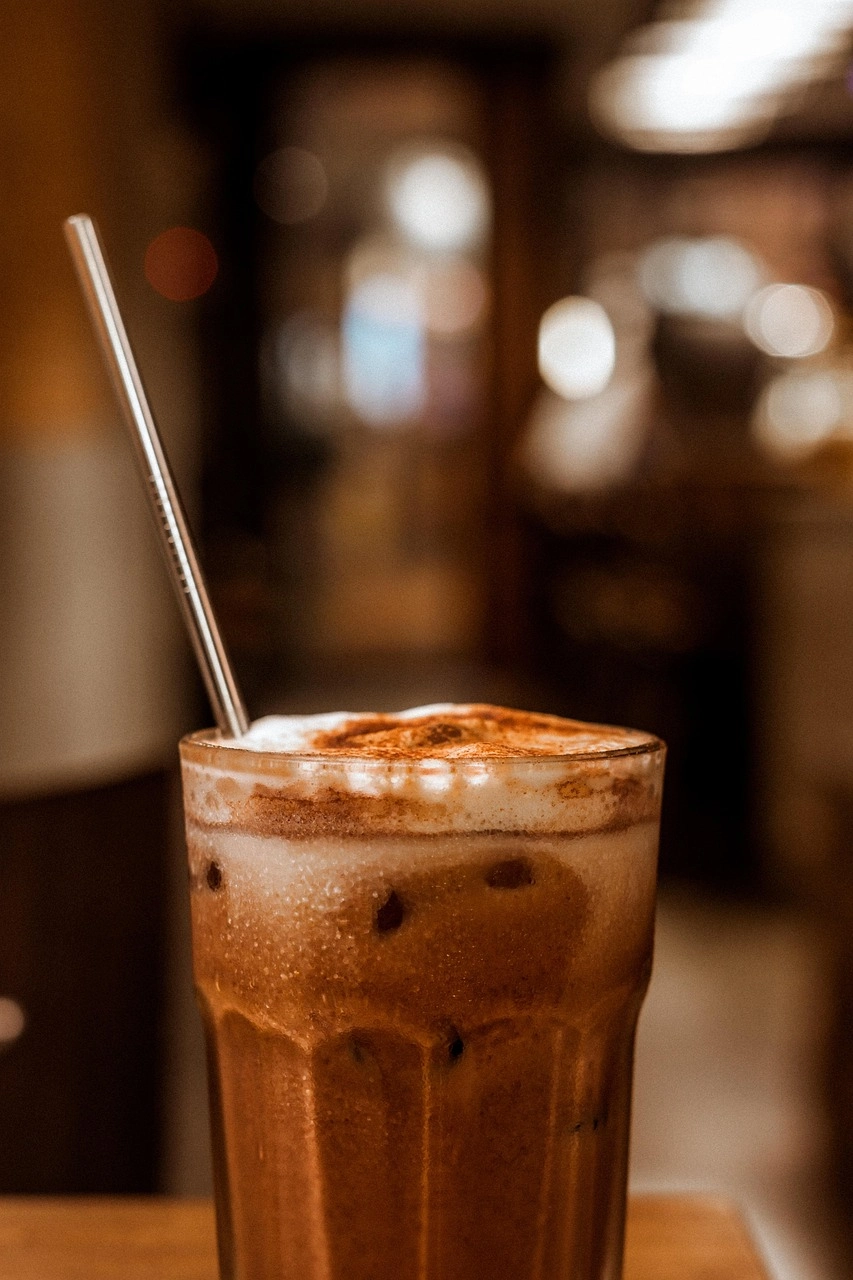 Nahaufnahme von Glas mit Kaffee mit Kakaopulver und Strohhalm