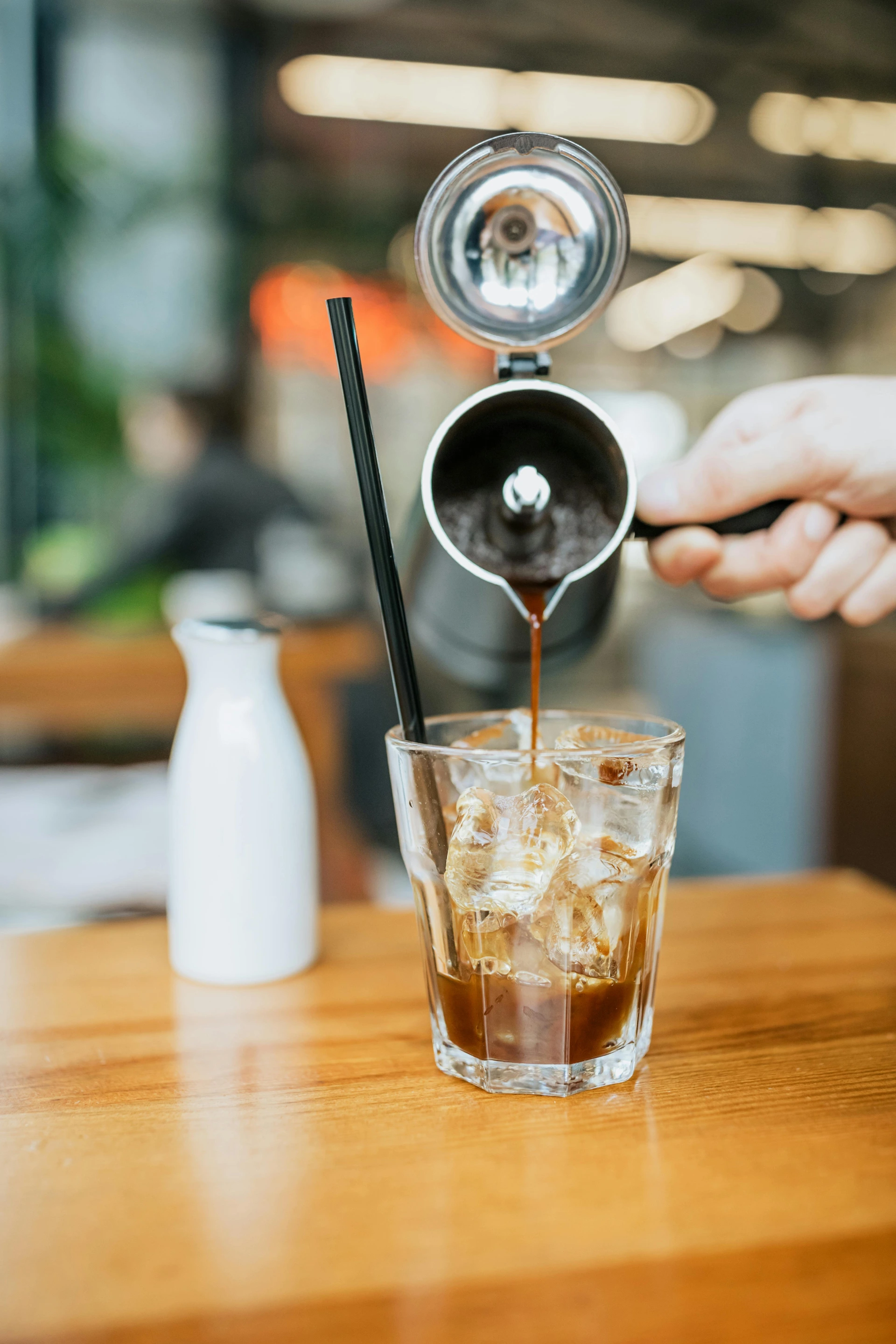 Kaffee beim Eingiessen über Eiswürfel im Glas mit Strohhalm