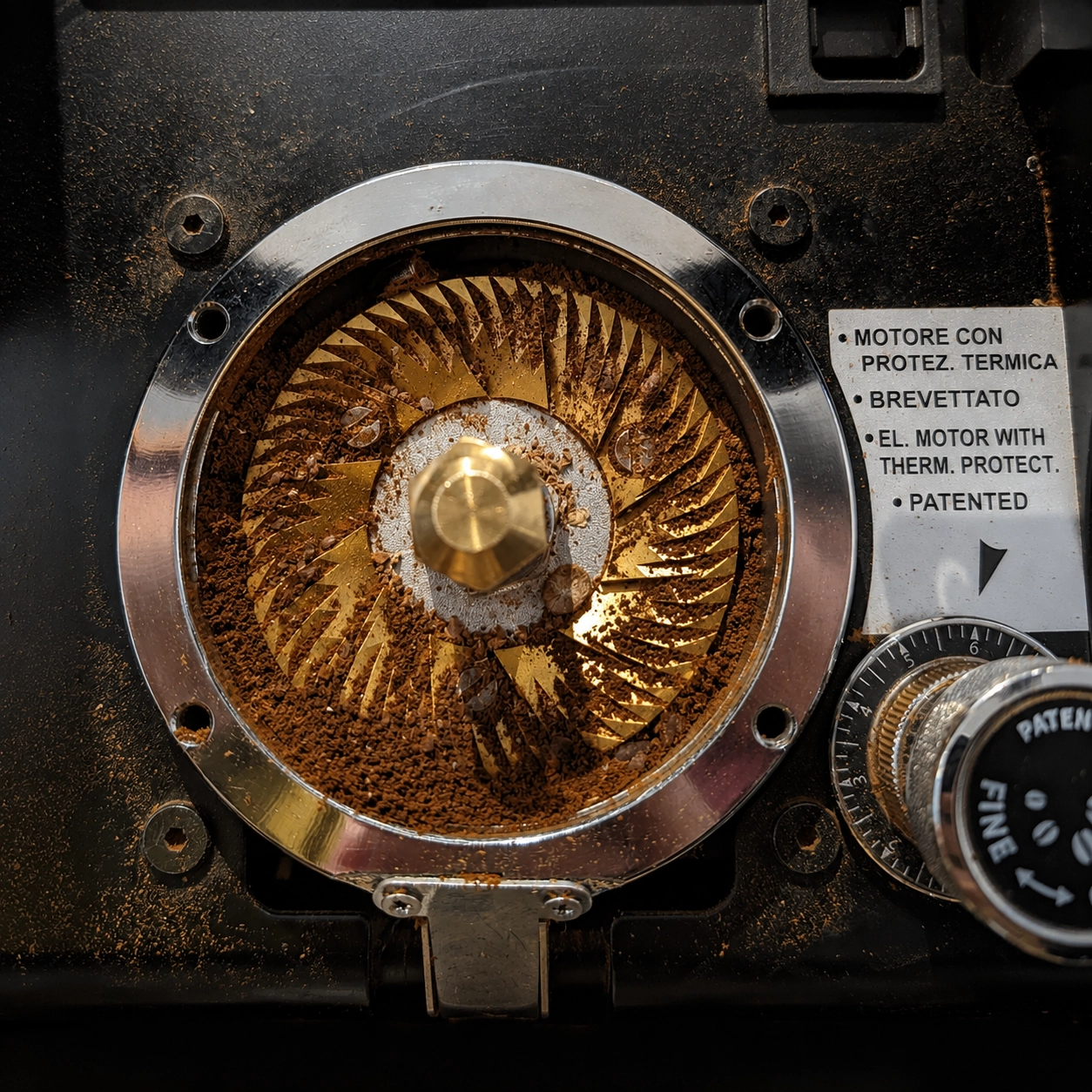 Nahaufnahme der geöffneten Mahlscheiben einer professionellen Kaffeemühle mit goldfarbenem Mahlwerk und reichlich frischem Kaffeepulver.